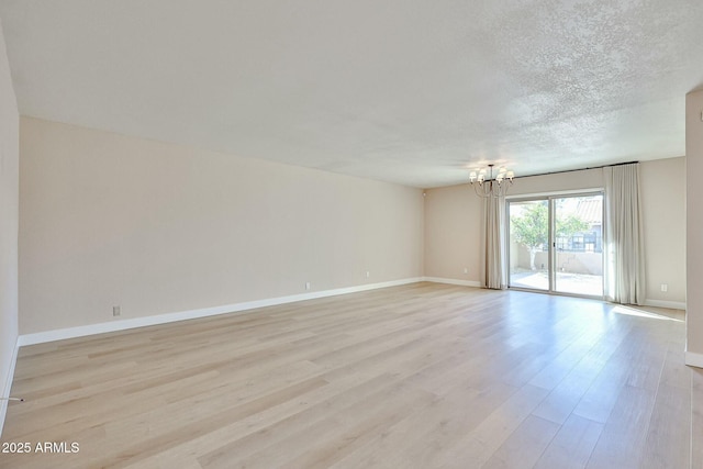 unfurnished room featuring light hardwood / wood-style floors, an inviting chandelier, and a textured ceiling