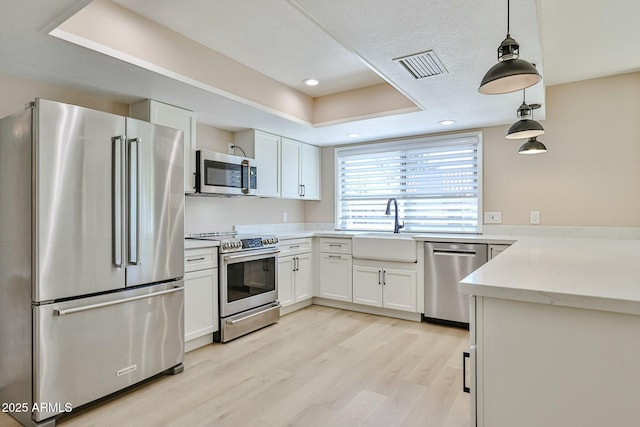 kitchen with sink, light wood-type flooring, white cabinetry, decorative light fixtures, and stainless steel appliances