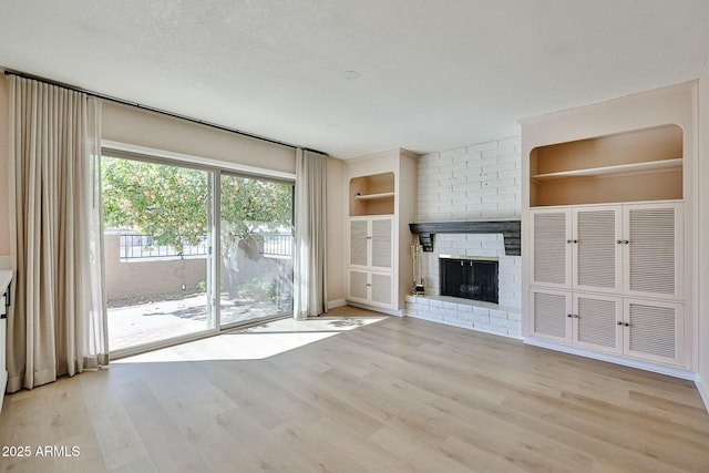 unfurnished living room featuring a textured ceiling, a brick fireplace, built in features, and light hardwood / wood-style flooring