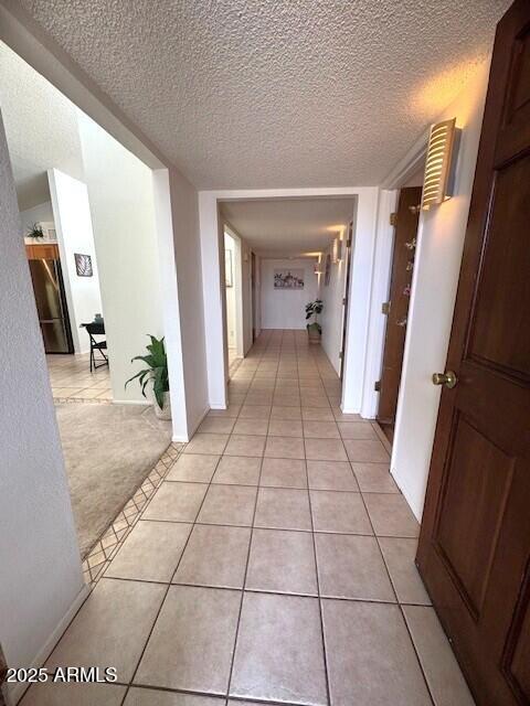 corridor with light tile patterned floors, a textured ceiling, and light colored carpet