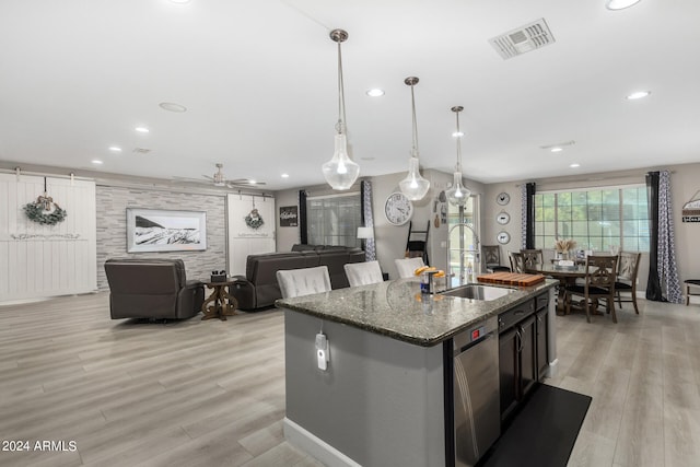 kitchen featuring dark stone countertops, sink, light wood-type flooring, and a center island with sink