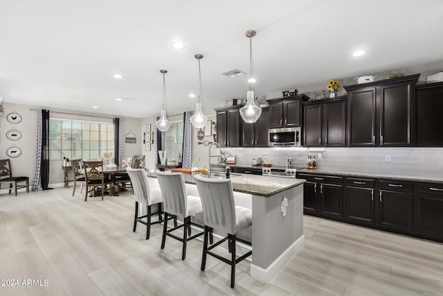 kitchen featuring light stone countertops, appliances with stainless steel finishes, a kitchen island with sink, and decorative light fixtures