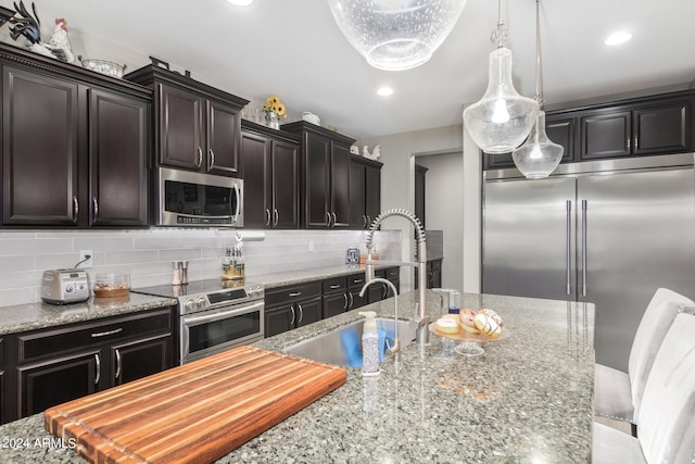 kitchen with tasteful backsplash, appliances with stainless steel finishes, hanging light fixtures, and light stone countertops