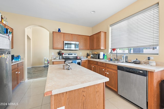 kitchen with light wood-type flooring, appliances with stainless steel finishes, a kitchen island, and sink