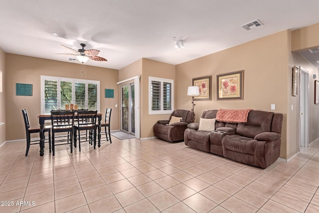 living area with light tile patterned floors, visible vents, baseboards, and a ceiling fan