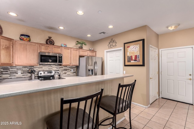 kitchen featuring visible vents, light tile patterned flooring, appliances with stainless steel finishes, a kitchen bar, and tasteful backsplash