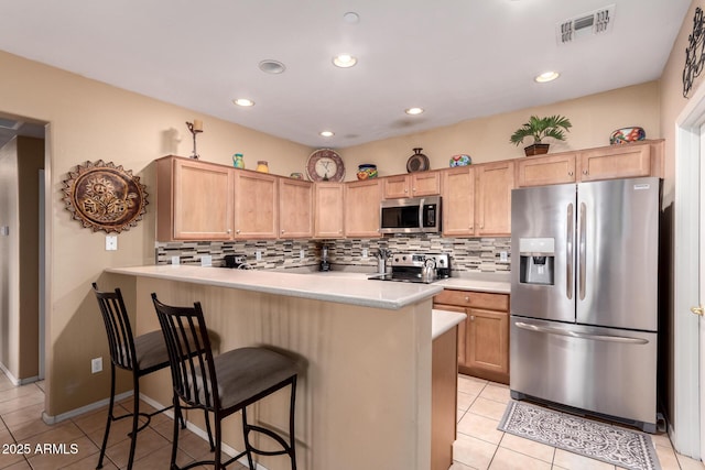 kitchen featuring visible vents, a kitchen breakfast bar, stainless steel appliances, and decorative backsplash