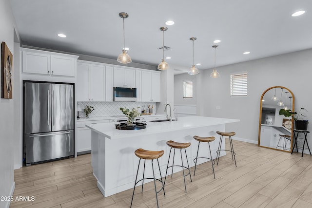 kitchen featuring stainless steel fridge, white cabinetry, and a kitchen island with sink