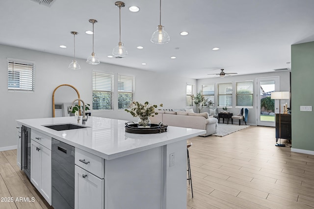 kitchen featuring ceiling fan, a kitchen island with sink, sink, black dishwasher, and hanging light fixtures