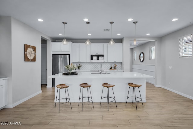 kitchen featuring decorative backsplash, a kitchen island with sink, white cabinets, and decorative light fixtures