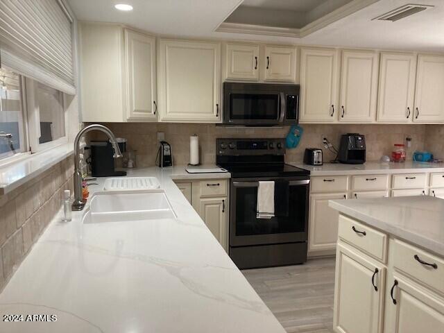 kitchen with stainless steel electric range, sink, decorative backsplash, a raised ceiling, and cream cabinetry