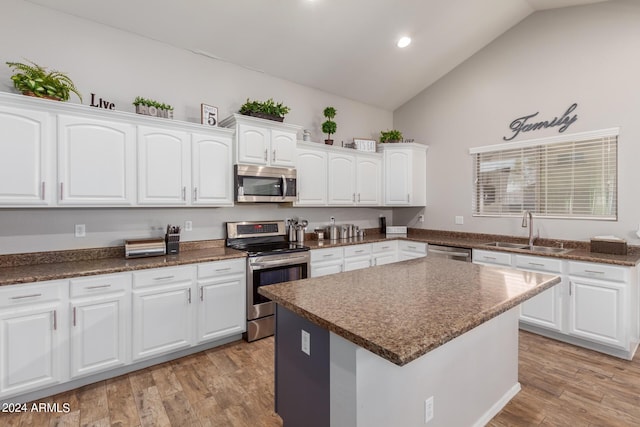 kitchen with lofted ceiling, a sink, white cabinets, light wood-style floors, and appliances with stainless steel finishes