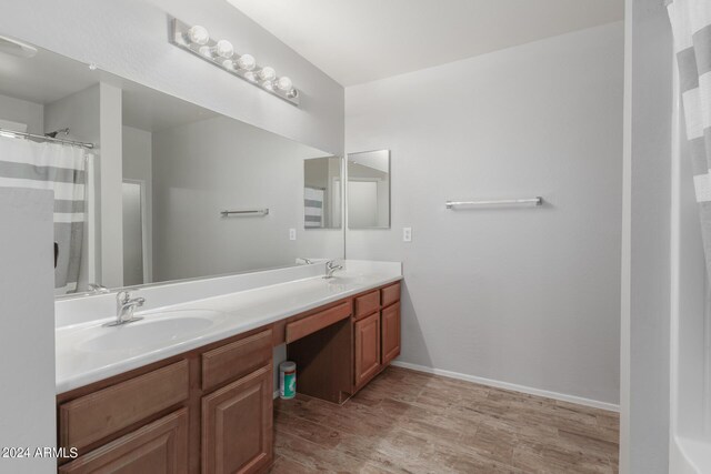 full bath with wood finished floors, a sink, baseboards, and double vanity