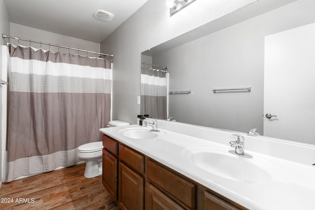 bathroom with double vanity, a sink, toilet, and wood finished floors