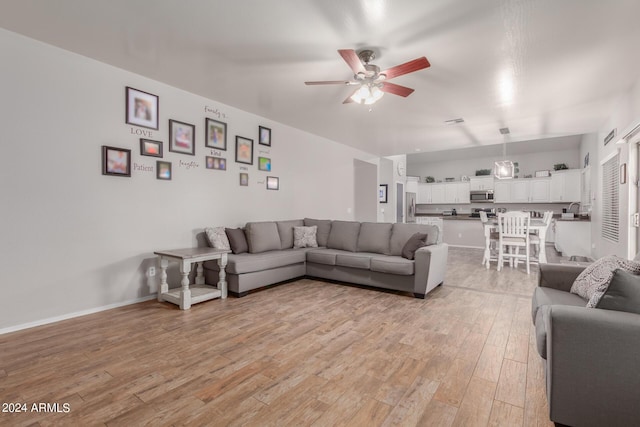 living area with ceiling fan, light wood-style flooring, and baseboards