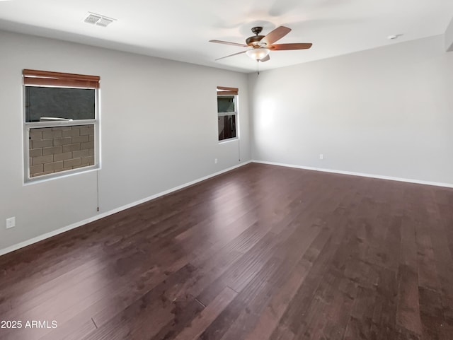 empty room with baseboards, ceiling fan, visible vents, and dark wood-type flooring