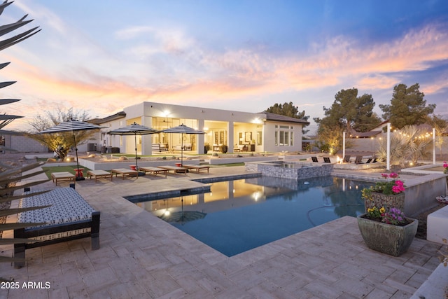 pool at dusk featuring a patio and an in ground hot tub