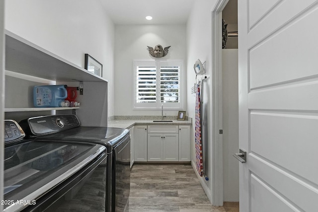 clothes washing area with separate washer and dryer, sink, light hardwood / wood-style flooring, and cabinets