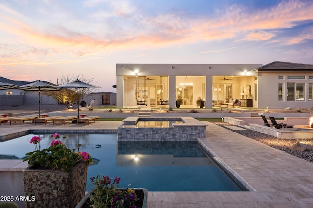 pool at dusk featuring an in ground hot tub, ceiling fan, a fire pit, and a patio