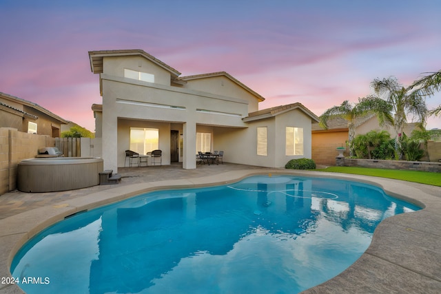 back house at dusk with a pool with hot tub and a patio area