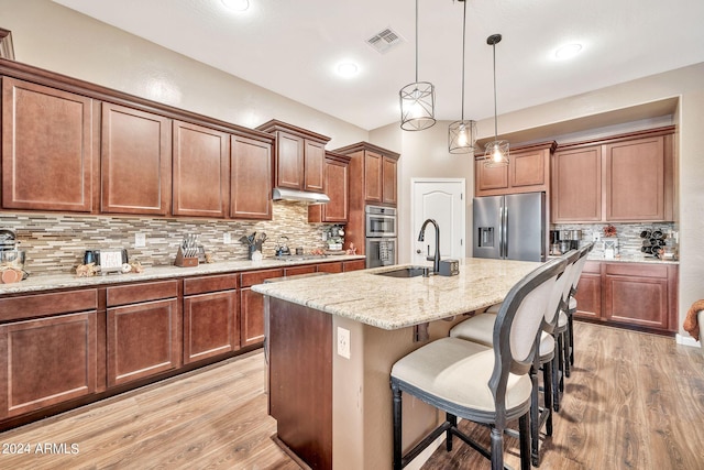 kitchen with pendant lighting, sink, light stone countertops, an island with sink, and appliances with stainless steel finishes