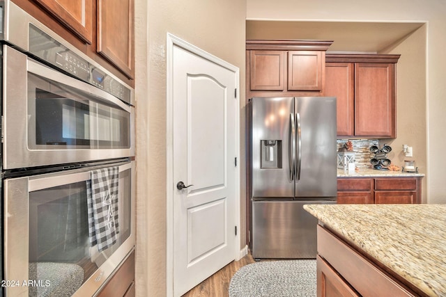 kitchen with light stone counters, light wood-type flooring, stainless steel appliances, and backsplash