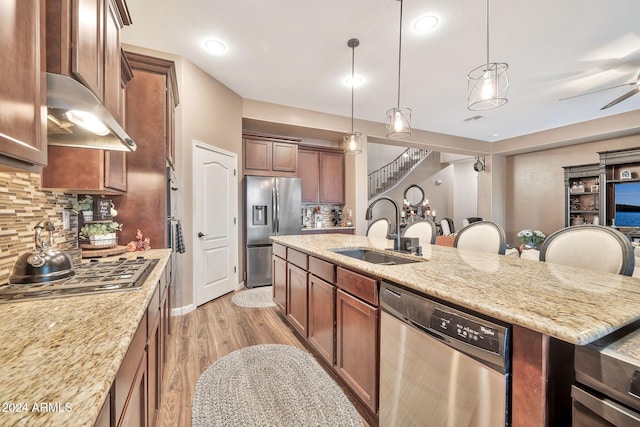 kitchen with light hardwood / wood-style flooring, sink, light stone counters, backsplash, and appliances with stainless steel finishes