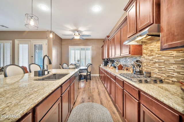 kitchen featuring light stone counters, sink, pendant lighting, stainless steel gas cooktop, and light hardwood / wood-style flooring