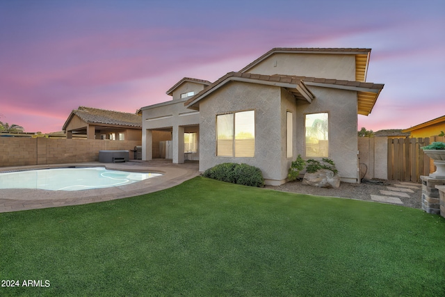 back house at dusk featuring a patio area and a lawn