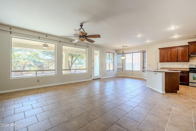 kitchen with hanging light fixtures, light tile patterned floors, an island with sink, stainless steel stove, and ceiling fan