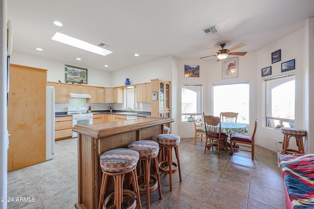 kitchen with a skylight, white appliances, ceiling fan, light brown cabinets, and a breakfast bar area