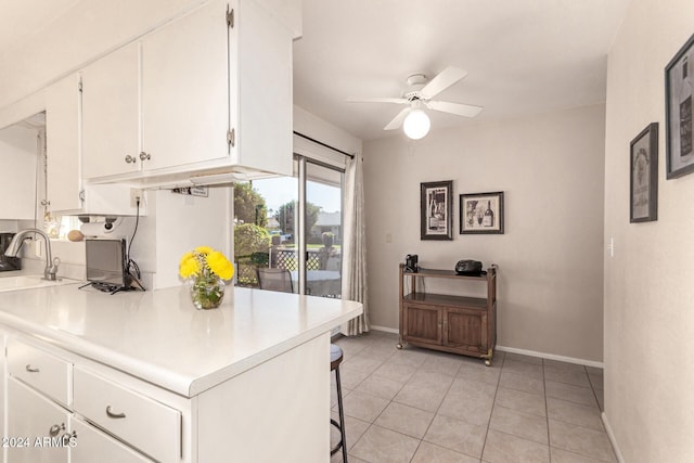 kitchen featuring ceiling fan, sink, light tile patterned flooring, a breakfast bar area, and white cabinets