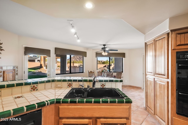 kitchen featuring sink, light tile patterned floors, ceiling fan, black double oven, and tile counters