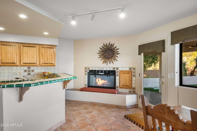 kitchen featuring a fireplace, tasteful backsplash, a kitchen bar, tile counters, and light tile patterned floors