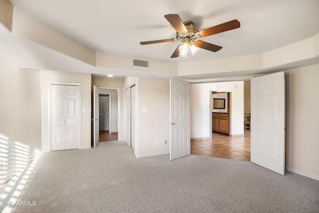 unfurnished bedroom featuring two closets, light colored carpet, and ceiling fan