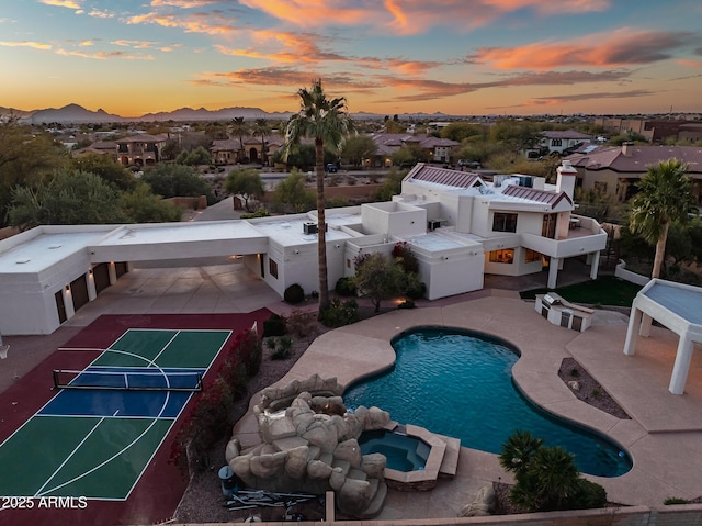 pool at dusk featuring a mountain view, tennis court, and basketball court