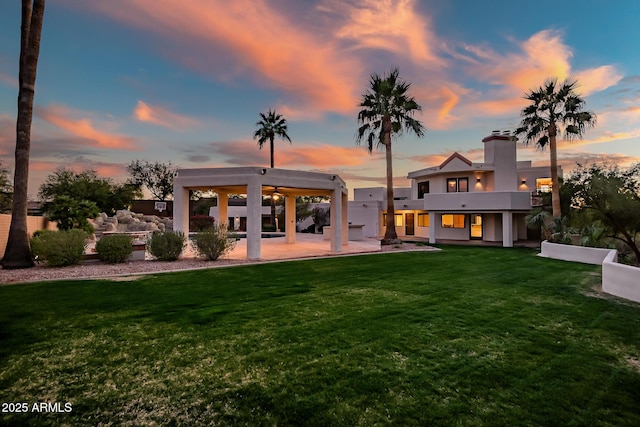 back house at dusk featuring a yard, a patio area, and a balcony