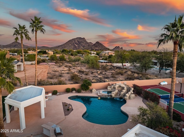 pool at dusk featuring a mountain view, a patio area, and tennis court