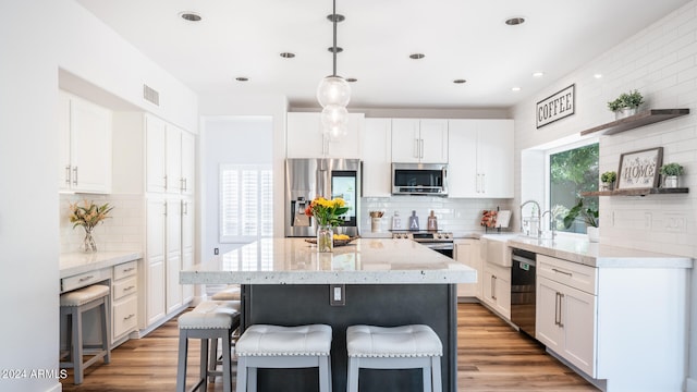 kitchen with appliances with stainless steel finishes, hardwood / wood-style floors, white cabinetry, and hanging light fixtures