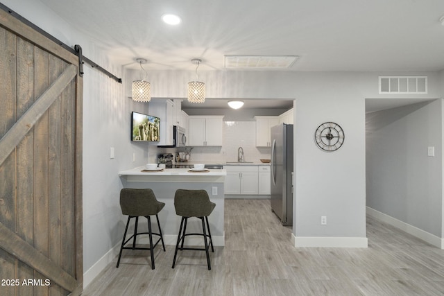 kitchen featuring a sink, stainless steel appliances, a barn door, a peninsula, and white cabinets