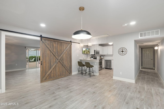 kitchen with appliances with stainless steel finishes, light countertops, a barn door, light wood-type flooring, and a breakfast bar area