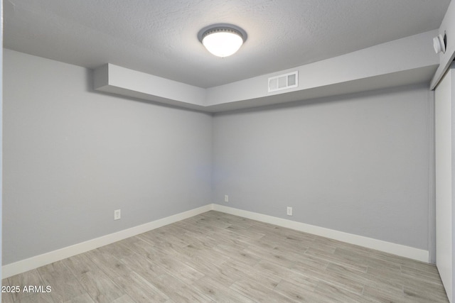 spare room with light wood-type flooring, baseboards, and a textured ceiling