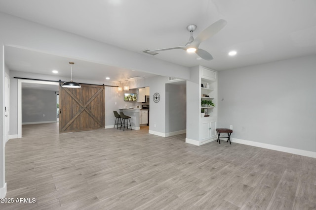 unfurnished living room with a barn door, ceiling fan, light wood-type flooring, recessed lighting, and baseboards