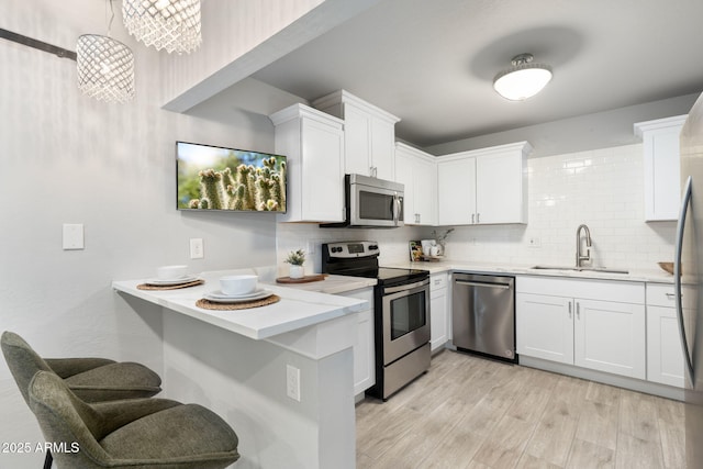 kitchen with stainless steel appliances, a sink, a peninsula, a kitchen bar, and white cabinetry