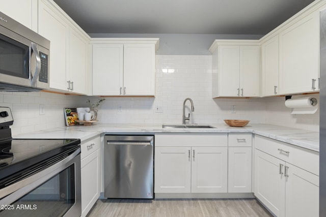 kitchen featuring stainless steel appliances, a sink, backsplash, and white cabinets