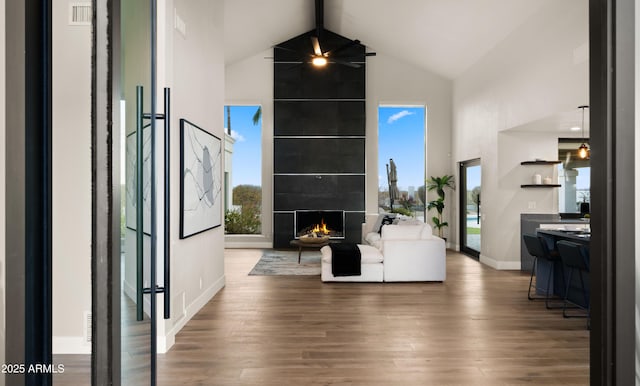 living room featuring ceiling fan, beam ceiling, a large fireplace, dark wood-type flooring, and high vaulted ceiling