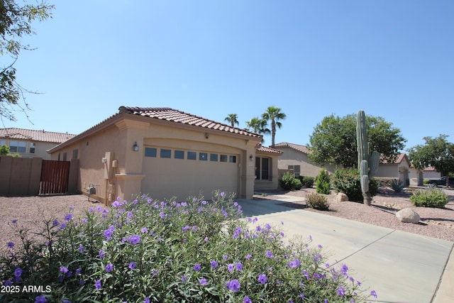 mediterranean / spanish home with a tile roof, stucco siding, concrete driveway, an attached garage, and fence