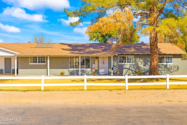 ranch-style home with a shingled roof, roof mounted solar panels, a fenced front yard, and stucco siding