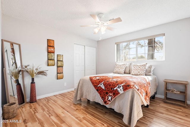 bedroom featuring a closet, light wood-style flooring, a textured ceiling, and baseboards