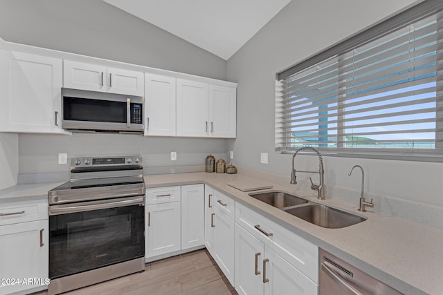 kitchen featuring sink, white cabinetry, stainless steel appliances, vaulted ceiling, and light hardwood / wood-style flooring